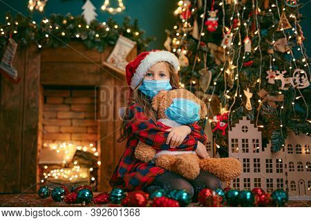 Portrait Of Cutel Little Child Girl In Medical Mask Playing With Taddy Bear, New Year Holiday Concep