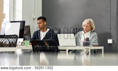 Aged Woman, Senior Intern Looking Uncertain While Using Laptop, Sitting At Desk, Working In Modern O