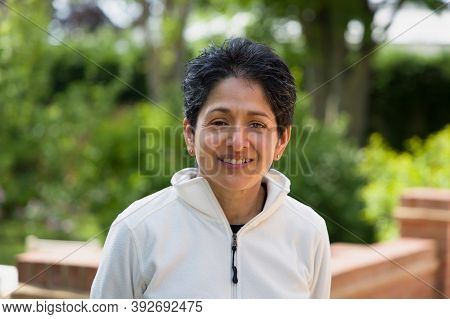 Casual Portrait Of An Indian Woman Smiling. British Asian (bame) Standing Outdoors In A Garden, Uk
