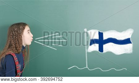 Pre-adolescent Girl Blowing On The School Board Drawn On The Blackboard Finland Flag. High Resolutio