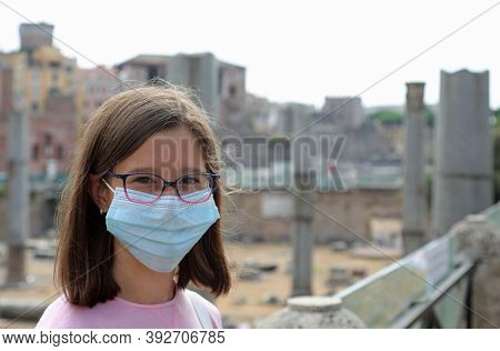 Young Girl With Surgical Mask While Visiting The City Of Rome In Italy And The Ruins Of Ancient Trai