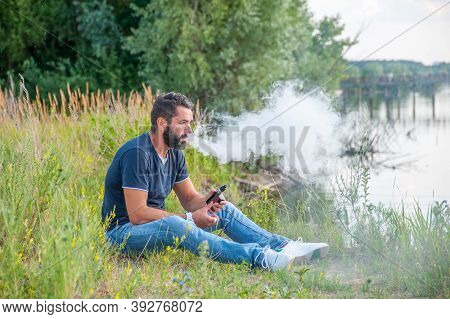Confident Vape Man Smoking An Vape In A Forest Clearing. Man Really Likes Process Of Smoking.