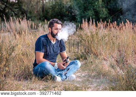 Stylish Bearded Vape Man Enjoying An Electronic Cigarette In The Forest. The New Technology Cigarett