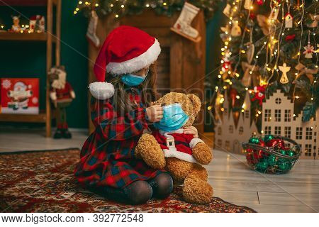 Portrait Of Cutel Little Child Girl In Medical Mask Playing With Taddy Bear, New Year Holiday Concep