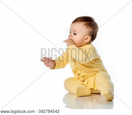 Little Baby Child In Yellow Jumpsuit With Hand In Mouth Scratching First Teeth. Teething, Oral Care 