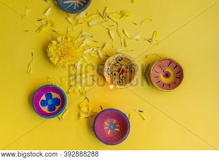 Few hand painted earthen Diwali lamps placed on bright yellow background. DIY project or craft for Diwali celebrations.