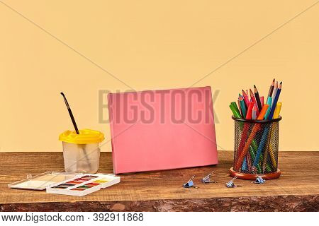 Pink Canvas, Watercolor, Paintbrush, Binder Clips, Felt-tip Pens And Colorful Pencils On Wooden Desk