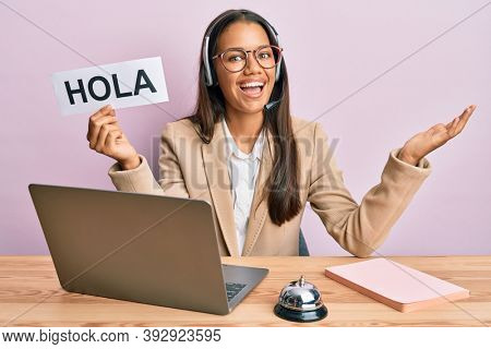Beautiful hispanic woman wearing operator headset holding hola greenting celebrating achievement with happy smile and winner expression with raised hand 