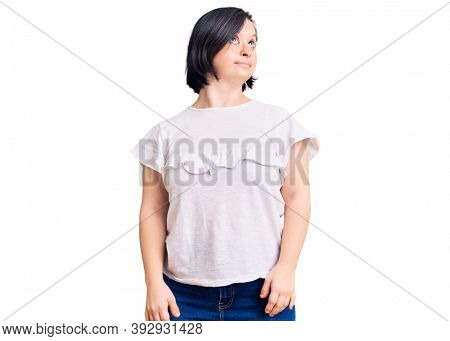 Brunette woman with down syndrome wearing casual white tshirt smiling looking to the side and staring away thinking. 