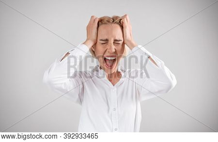 Mature Business Lady Clenching Her Head And Shouting In Anger On Light Grey Studio Background. Femal