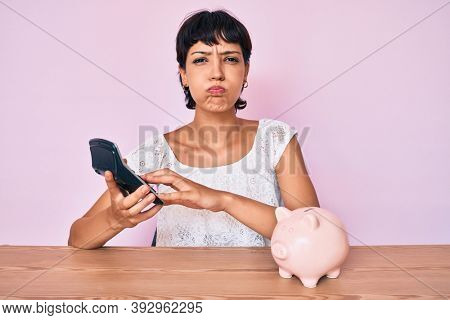 Beautiful brunettte woman caculating money savings puffing cheeks with funny face. mouth inflated with air, catching air. 