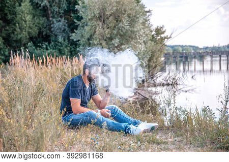 Stylish Vaper Blows Up A Couple An Electronic Cigarette In A Forest Clearing. Alternative To Smoking
