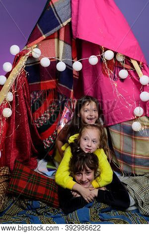 Kids Embrace In Home-made Tent Inside The Living Room Before Going To Sleep. Child Pajama Party. Paj