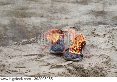 Burning Sports Sneakers Or Gym Shoes On Fire Stand On Sandy Beach Coast. Athlete Burned Out. Physica