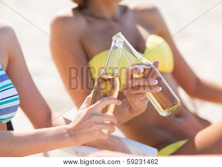 summer holidays and vacation - two girls in bikinis with drinks on the beach chairs