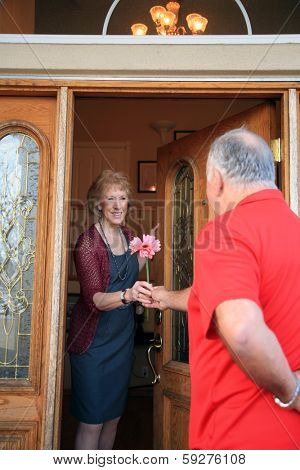 A very handsome and romantic man surprises his gorgeous wife with flowers and candy for Valentines Day at the front door. The perfect Valentines Day image for all your senior citizen love needs. 