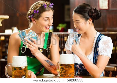 In Pub - friends in Tracht, Dirndl and Lederhosen drinking a fresh beer in Bavaria, Germany playing cards
