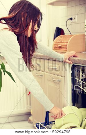 Young woman in kitchen doing housework. Puling out dishes from dishwasher