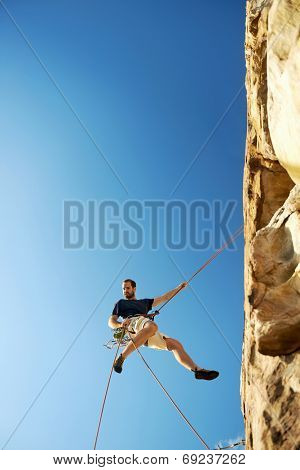 A rock climber going down a steep mountain with a rope against a blue sky
