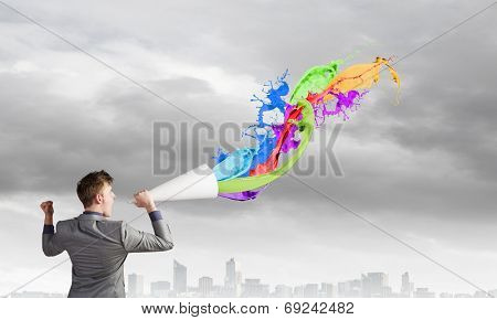 Young businessman speaking in trumpet and colorful splashes flying out