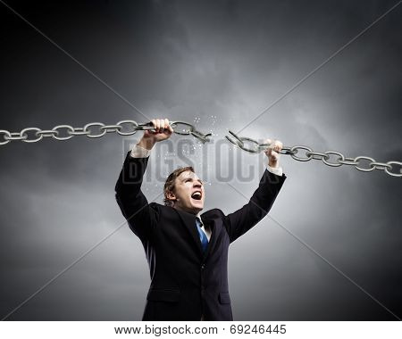 Young furious businessman breaking metal chain with hands