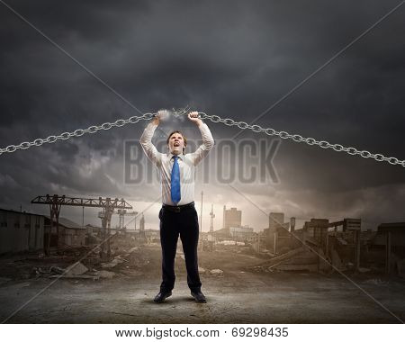 Young furious businessman breaking metal chain with hands