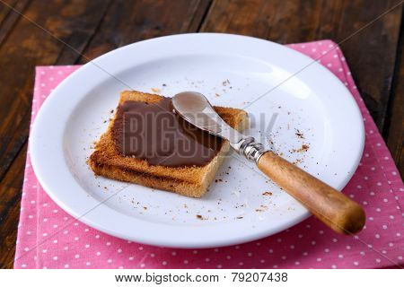 Toast bread spread with chocolate on plate with knife and napkin on wooden table background