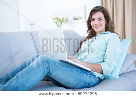 Happy brunette using her laptop on couch at home in the living room