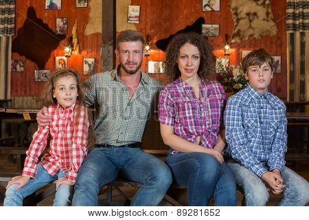family of four sitting on a bench on background of wall with pelts