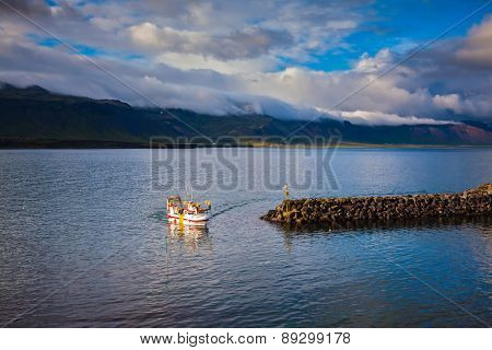 White fishing boat in the harbor pier fishing village Arnastapi. Sunset on the sea fjord in Iceland