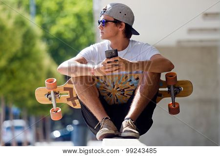 Handsome Skater Boy Using His Mobile Phone In The Street.