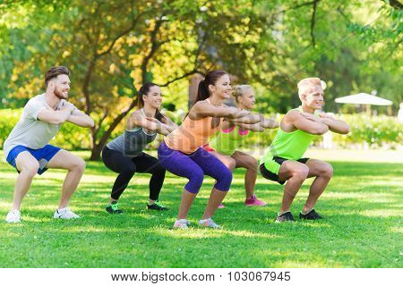 fitness, sport, friendship and healthy lifestyle concept - group of happy teenage friends or sportsmen exercising and doing squats at boot camp