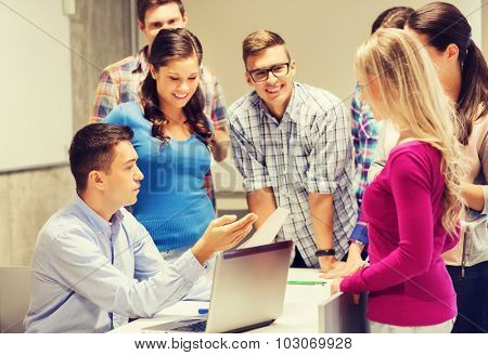 education, high school, technology and people concept - group of smiling students and teacher with papers, laptop computer in classroom