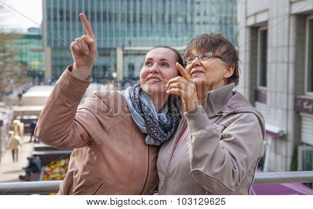 Outdoor family portrait of pension age Mother and her daughter in the city, smiling and looking arou