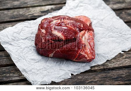 Raw Ox Cheek On Crumpled Paper,  On Old  Wooden Table