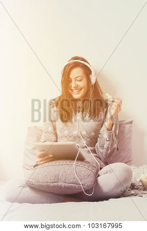 Young woman with tablet and headphones in bed