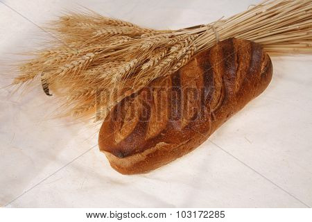 bunch of mown wheat ears with vintage handmade reaper hook sickle and rye dark white french fresh bread loaf on light linen tablecloth