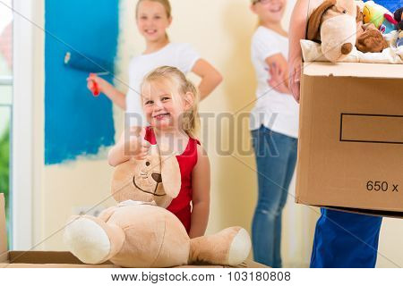 Family moving house with boxes full of stuff, they are painting the walls of their new home