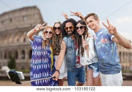 summer vacation, travel, tourism, technology and people concept - smiling young hippie friends taking picture by smartphone selfie stick over coloseum background