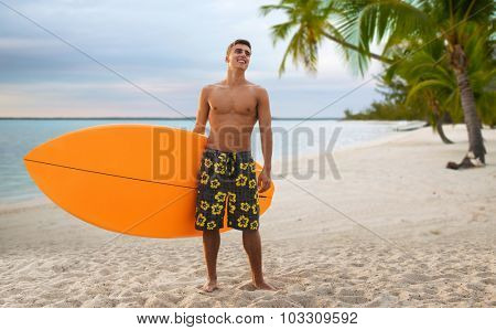summer vacation, people, travel and water sport concept - smiling young man with surfboard or stand up paddle board over tropical beach and palm trees beach background