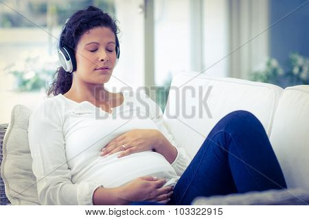 Pregnant woman with headphones relaxing on sofa at home