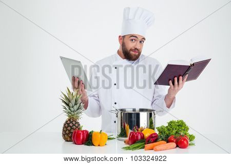 Portrait of a young male chef cook holding tablet computer and receipe book isolated on a white background
