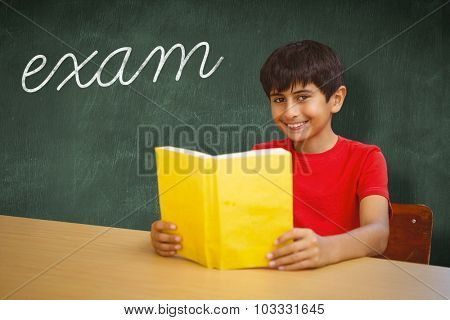 The word exam and portrait of boy reading book in library against green chalkboard