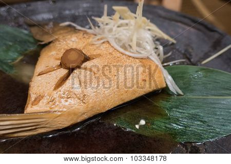 Hamachi cooked in sauce on black ceramic plate