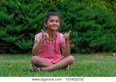 Little Child Gypsy Girl Showing Thumbs Up Sitting In Grass And Smiling