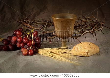 Wine cup surrounded by bread and grapes with crown of thorns in background as symbols of communion