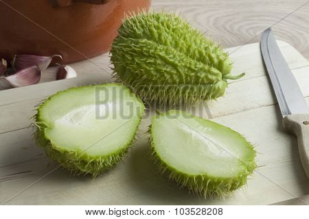 Whole and half spined fresh chayote fruit on a cutting board