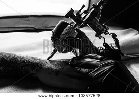 Tattooist makes tattoo on clients arm in bw