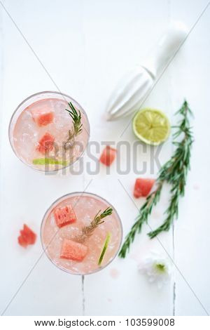 Light pink cocktails mocktail drinks decorated with cut up watermelon and rosemary with a flower and a piece of lime beside it