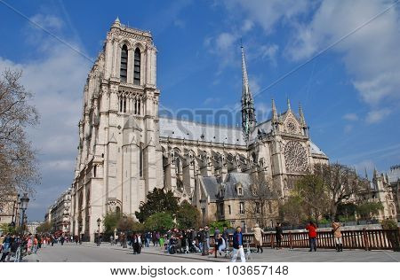 PARIS, FRANCE - MARCH 18, 2014: People walk across the Pont au Double in front of the historic Notre Dame cathedral. Started in 1120, the Catholic cathedral was completed in 1345.